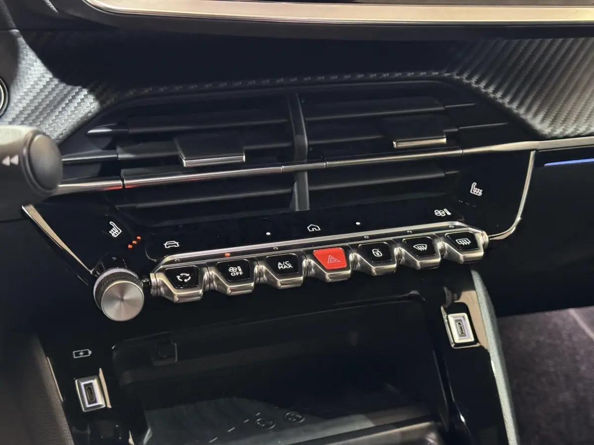 Gros plan sur la console centrale noire brillante de la Peugeot 208 Hybrid 136, avec boutons chromés et écran tactile.