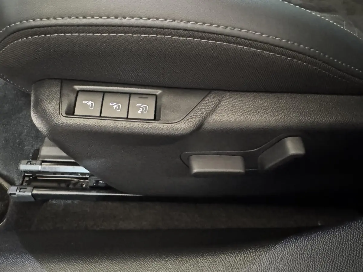 Détail des commandes de réglage électrique du siège avant côté conducteur, tissu noir avec surpiqûres grises.