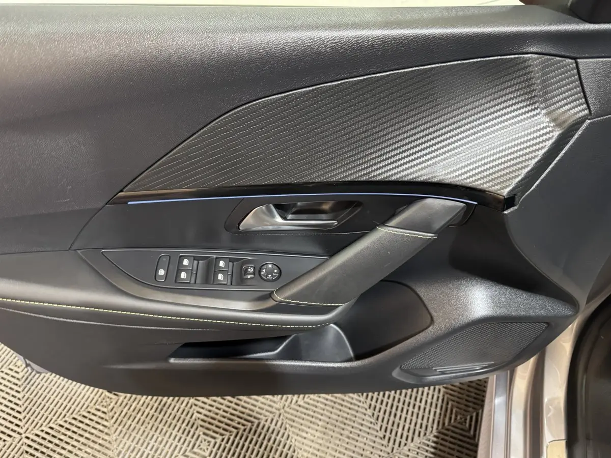 Gros plan sur la porte côté conducteur de la Peugeot 208 Hybrid gris clair, avec insert imitation carbone et commandes électriques.
