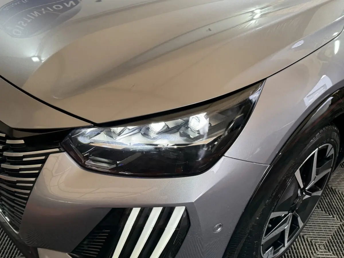 Gros plan sur l'avant droit gris clair du Peugeot 208 Hybrid 136 eDCS6 GT, avec phares LED et jante noire design.