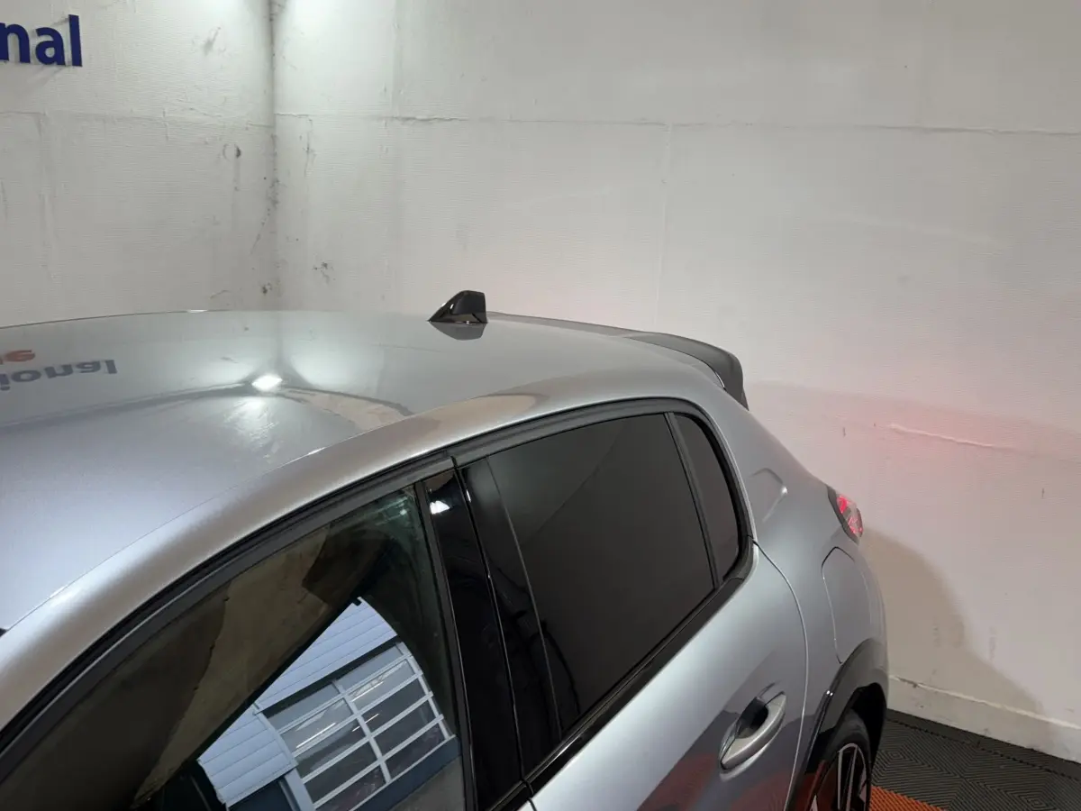 Vue 3/4 arrière droite d'une Peugeot 208 Hybrid 136 GT gris clair avec vitres teintées et antenne requin.