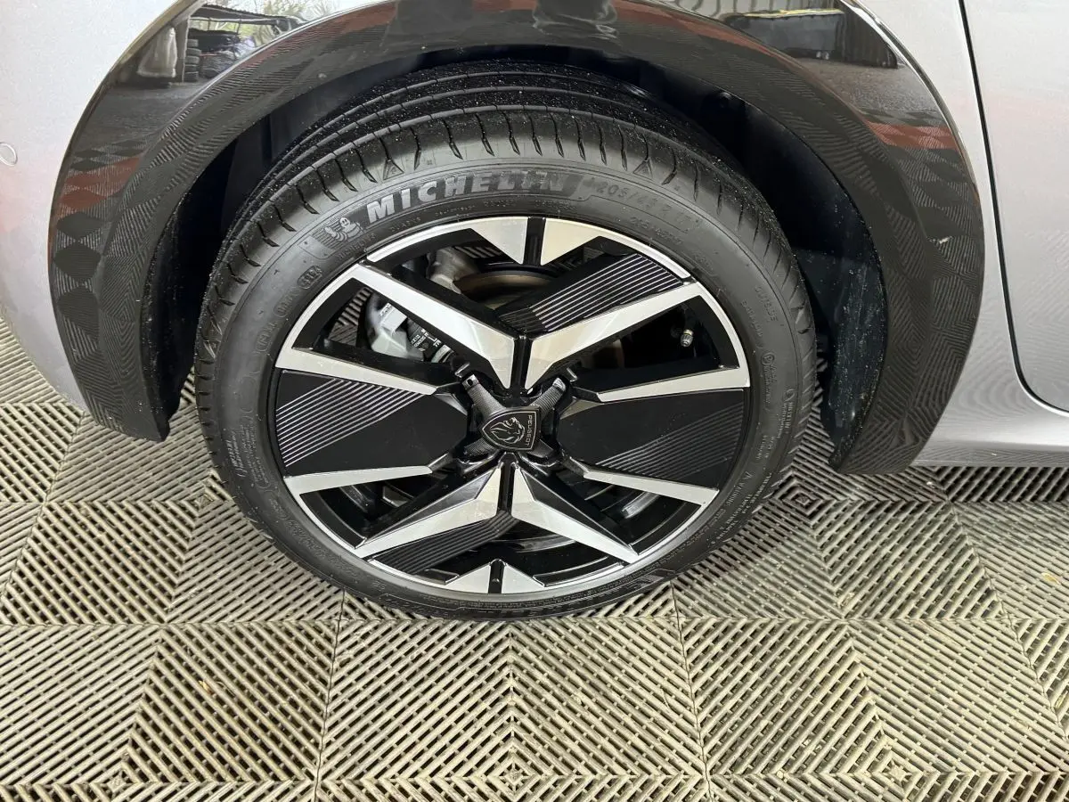 Gros plan sur la roue avant droite de la Peugeot 208 Hybrid 136 eDCS6 GT gris clair avec jante alliage noire et argent.