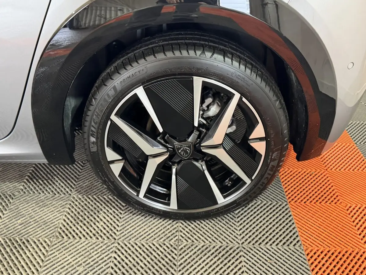 Gros plan sur la roue avant droite de la Peugeot 208 Hybrid gris clair avec jante alliage noire et argentée design moderne.