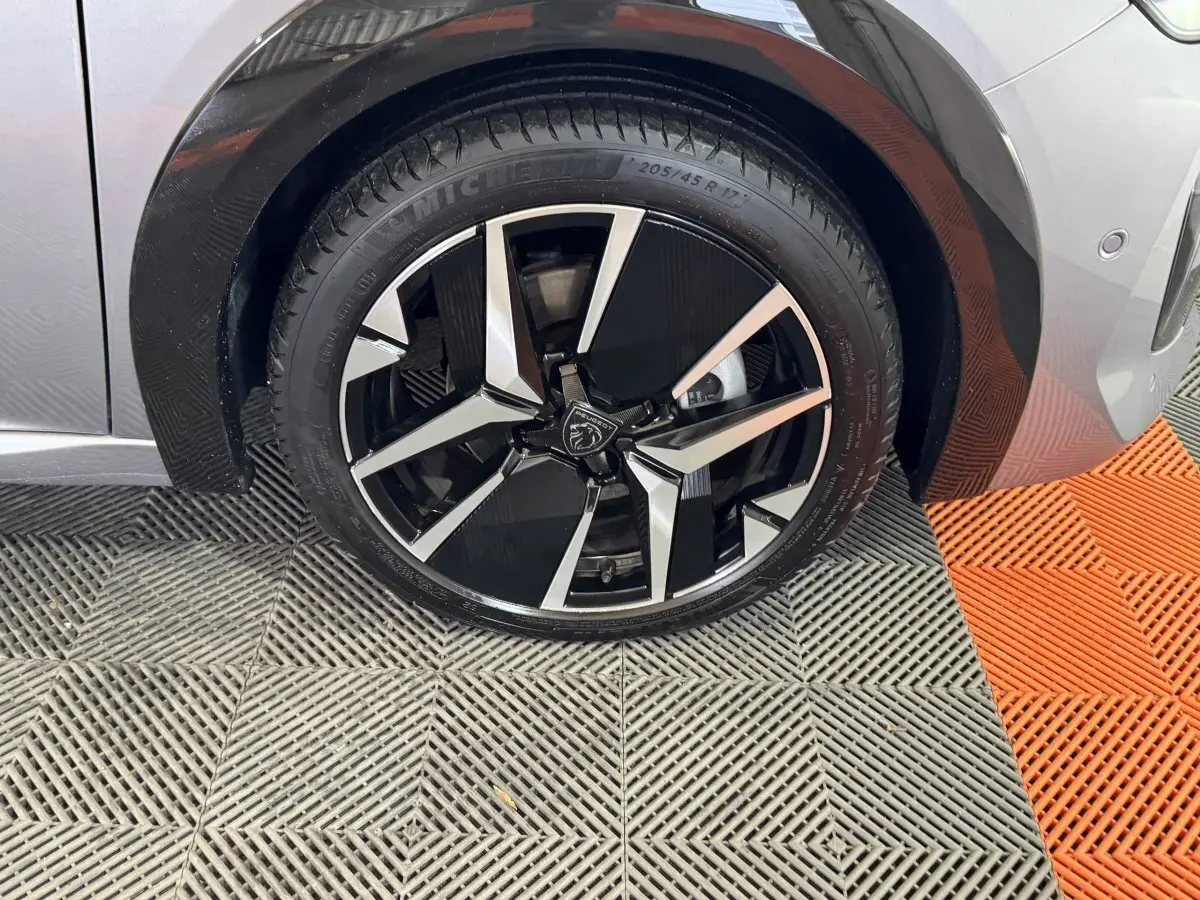 Gros plan sur la roue avant droite de la Peugeot 208 Hybrid 136 eDCS6 GT gris clair avec jante alliage noire et argent.
