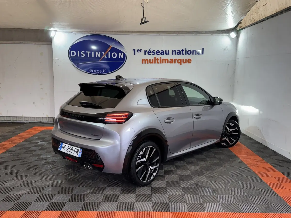 Peugeot 208 Hybrid gris clair vue 3/4 arrière droit dans un showroom avec sol à damiers noir et orange.