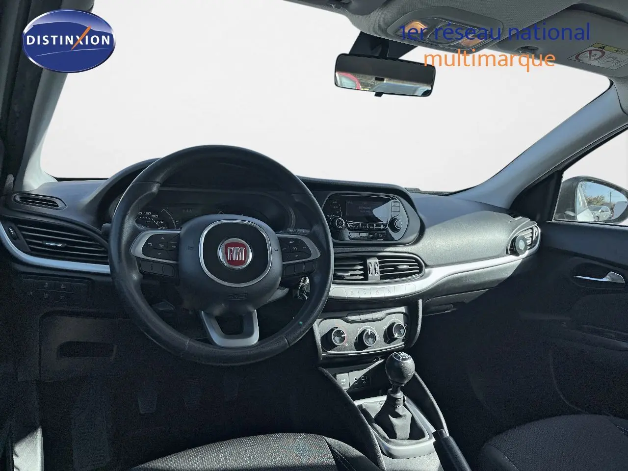 Intérieur de la Fiat Tipo 5 portes blanche, vue frontale sur le volant, tableau de bord et levier de vitesse manuel.