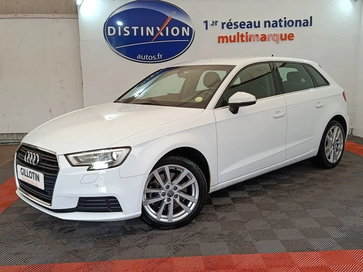Audi A3 blanc vue 3/4 avant droit, avec jantes alliage et phares LED, en intérieur showroom.