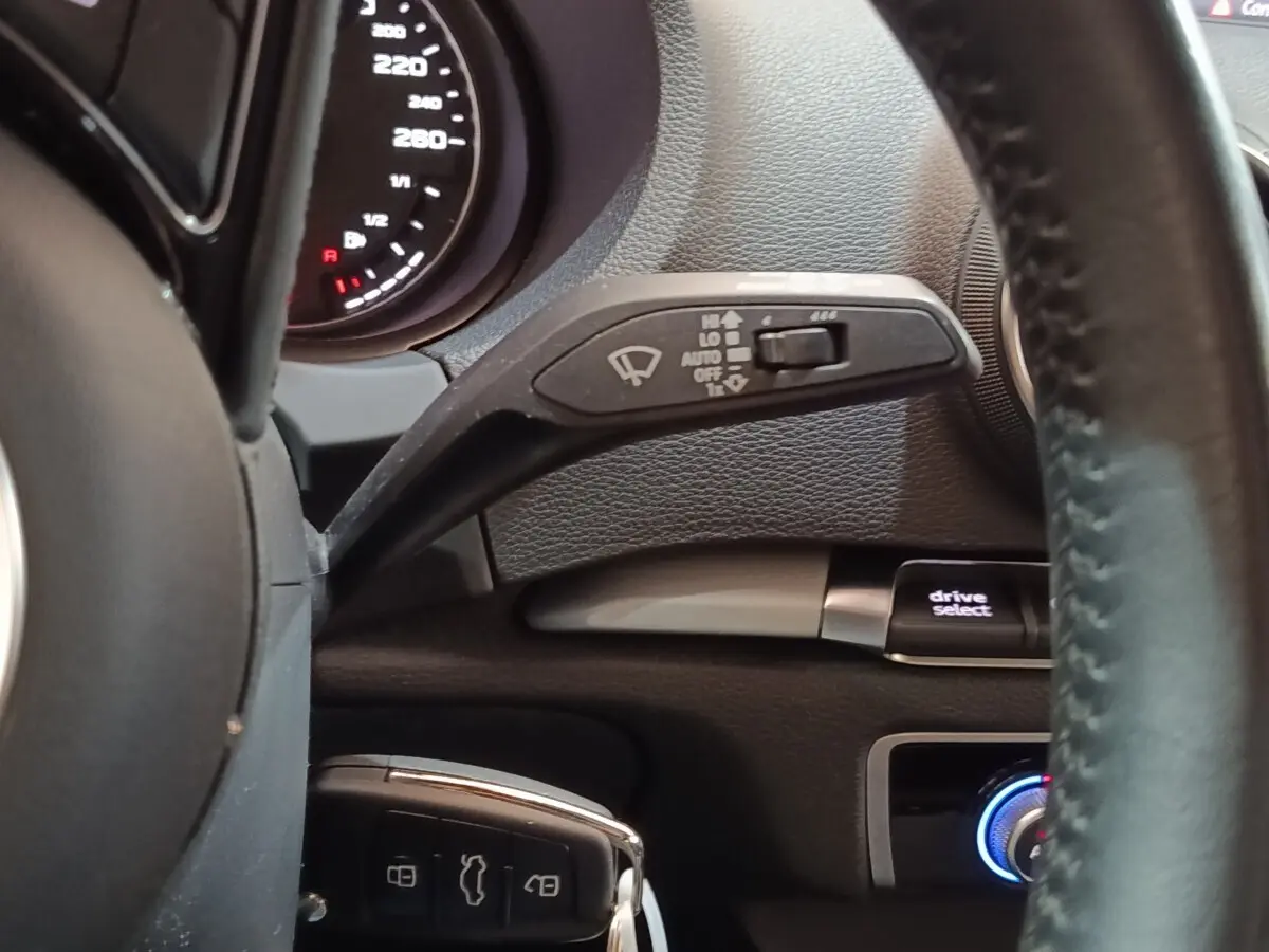 Vue rapprochée du volant cuir noir d’Audi A3 blanc 2020, avec commandes essuie-glace et bouton drive select visibles.
