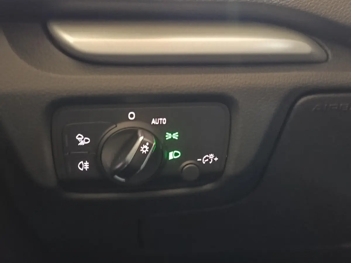Gros plan sur le bouton de commande des phares avec éclairage vert, tableau de bord noir de l'Audi A3 blanc.