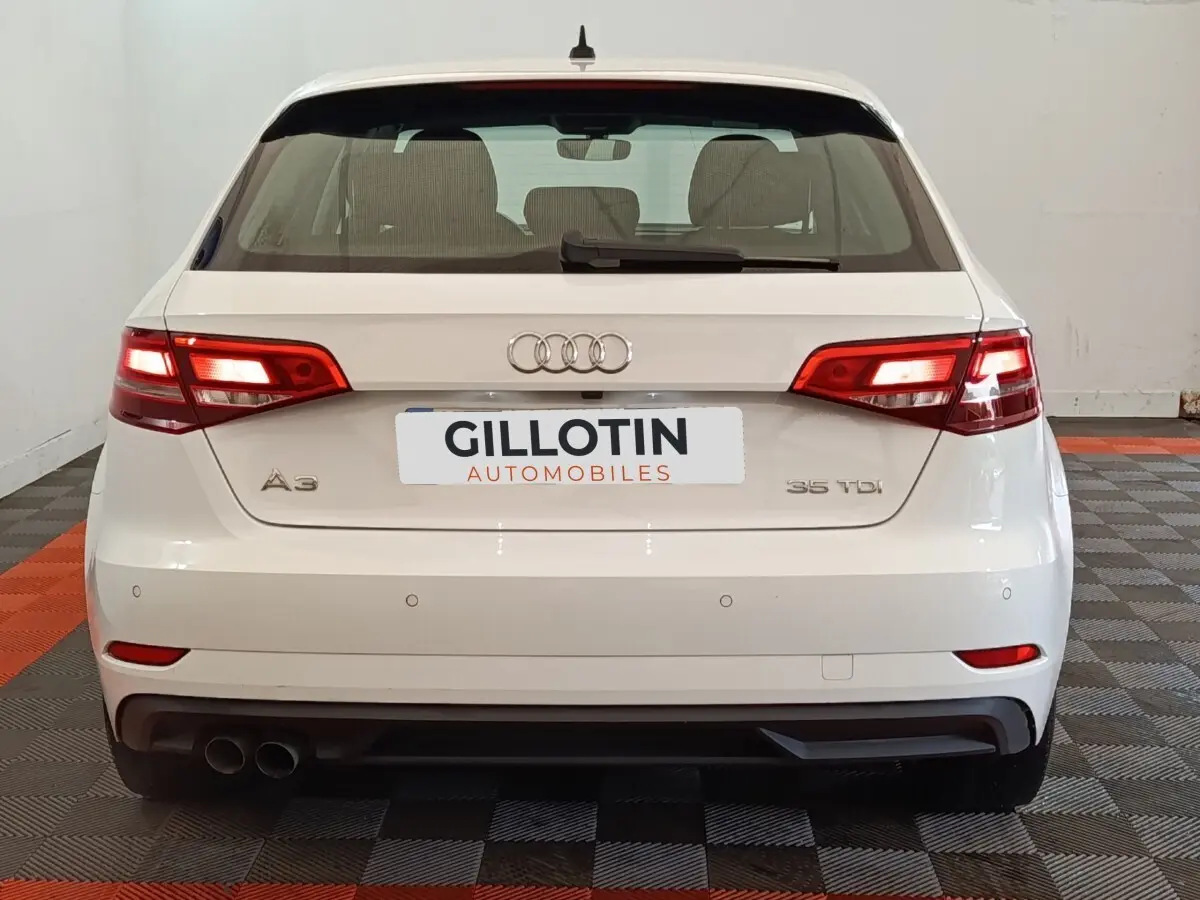 Vue arrière d'une Audi A3 35 TDI blanche avec feux allumés et double sortie d'échappement à gauche.