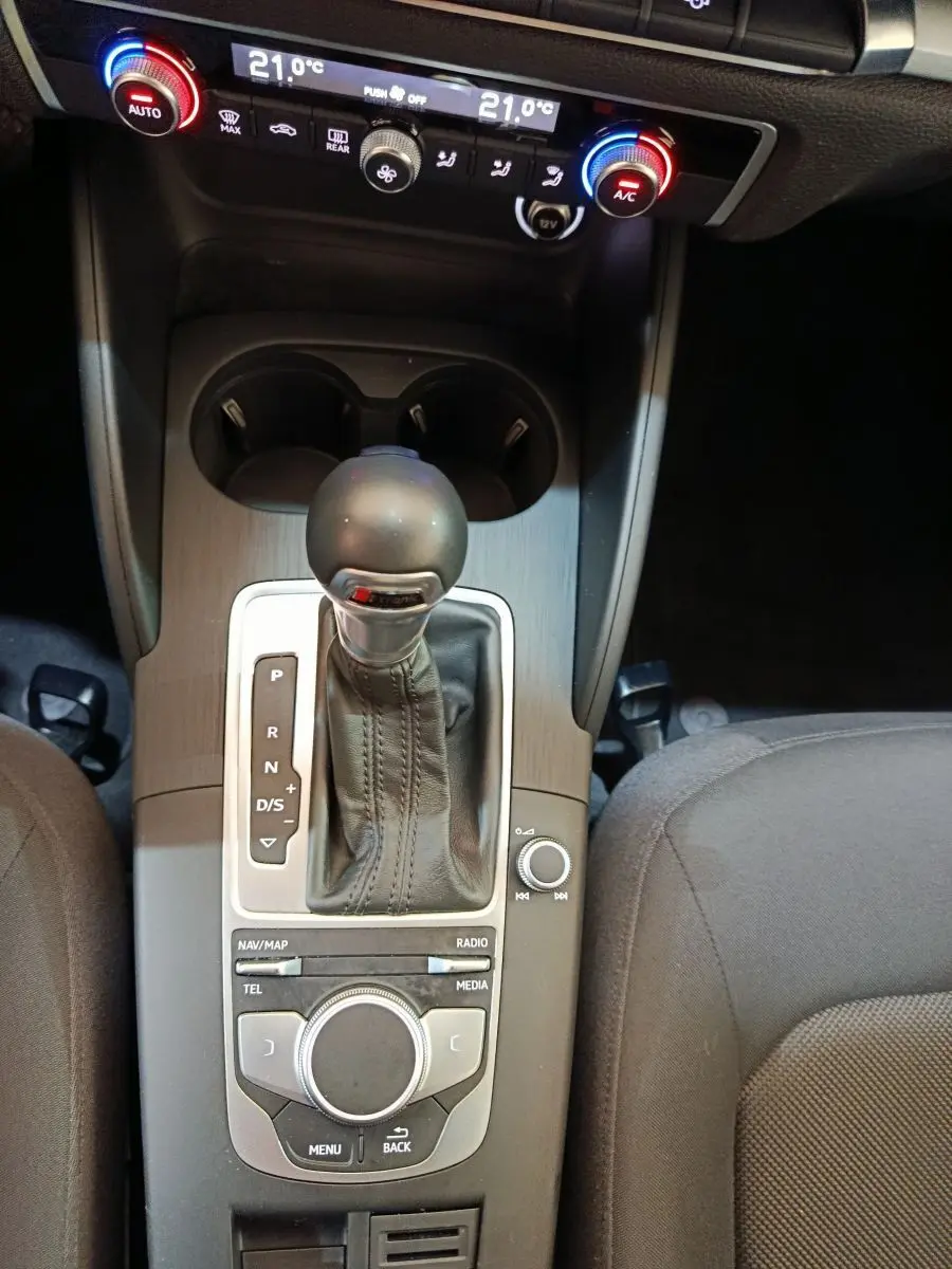 Vue rapprochée de la console centrale de l'Audi A3 blanche, mettant en valeur le levier de vitesse automatique et les commandes de climatisation.