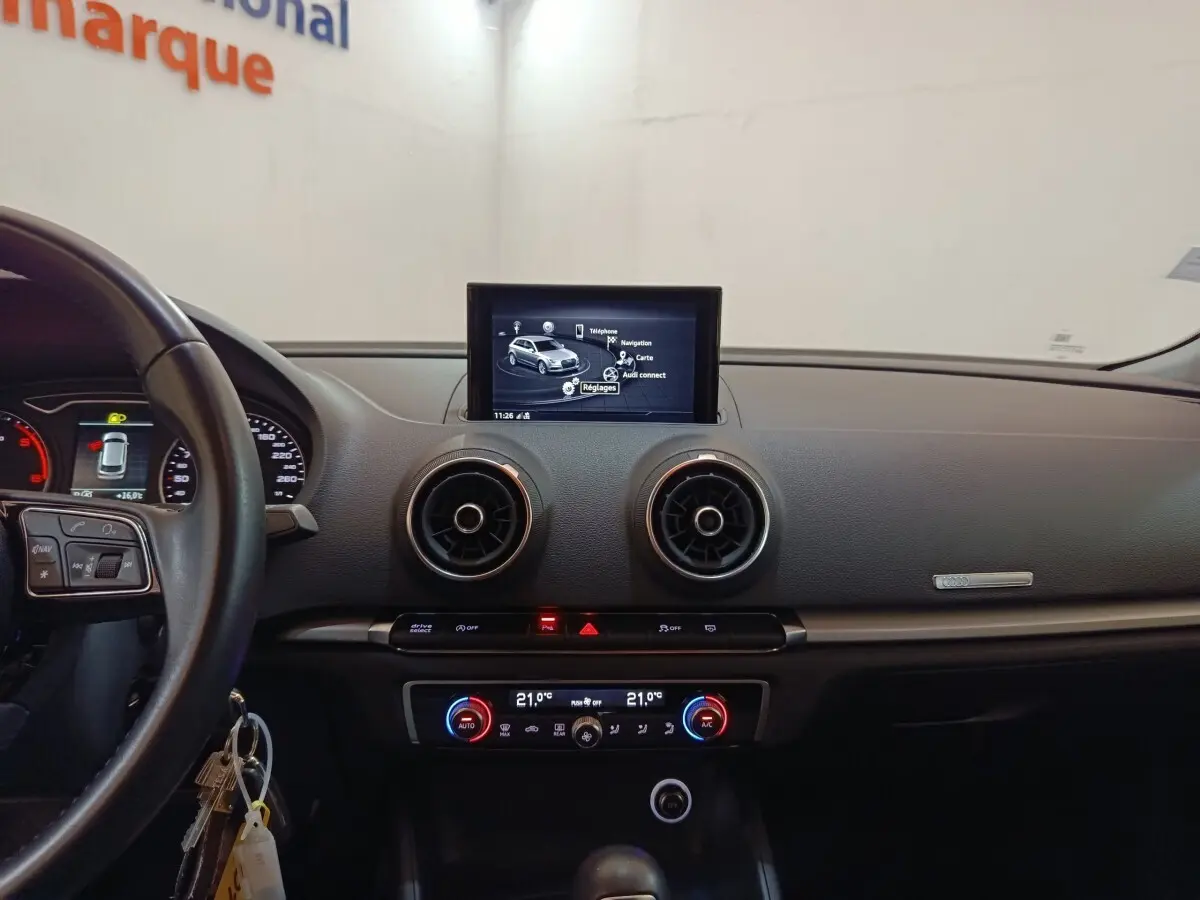 Vue intérieure du tableau de bord d'une Audi A3 35 TDI blanc, avec écran tactile central et commandes de climatisation digitales.