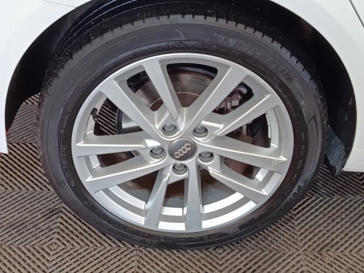 Gros plan sur la roue avant droite argentée d'une Audi A3 blanche, mettant en valeur la jante en alliage.