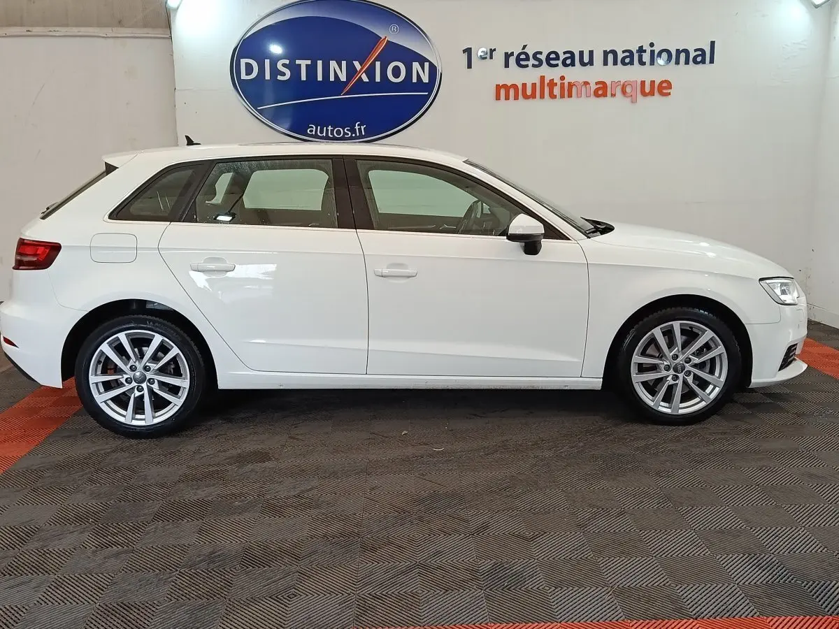 Audi A3 blanc vue de profil côté gauche, en intérieur, avec jantes alliage et logo Distinxion en arrière-plan.