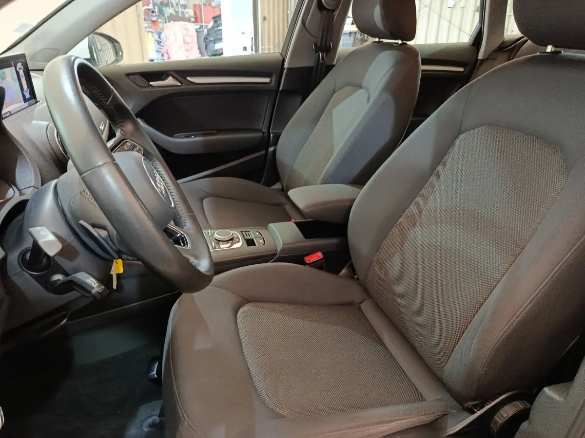 Vue intérieure côté conducteur de l'Audi A3 35 TDI 150 S tronic Business Line avec sièges tissu gris et volant cuir multifonctions.