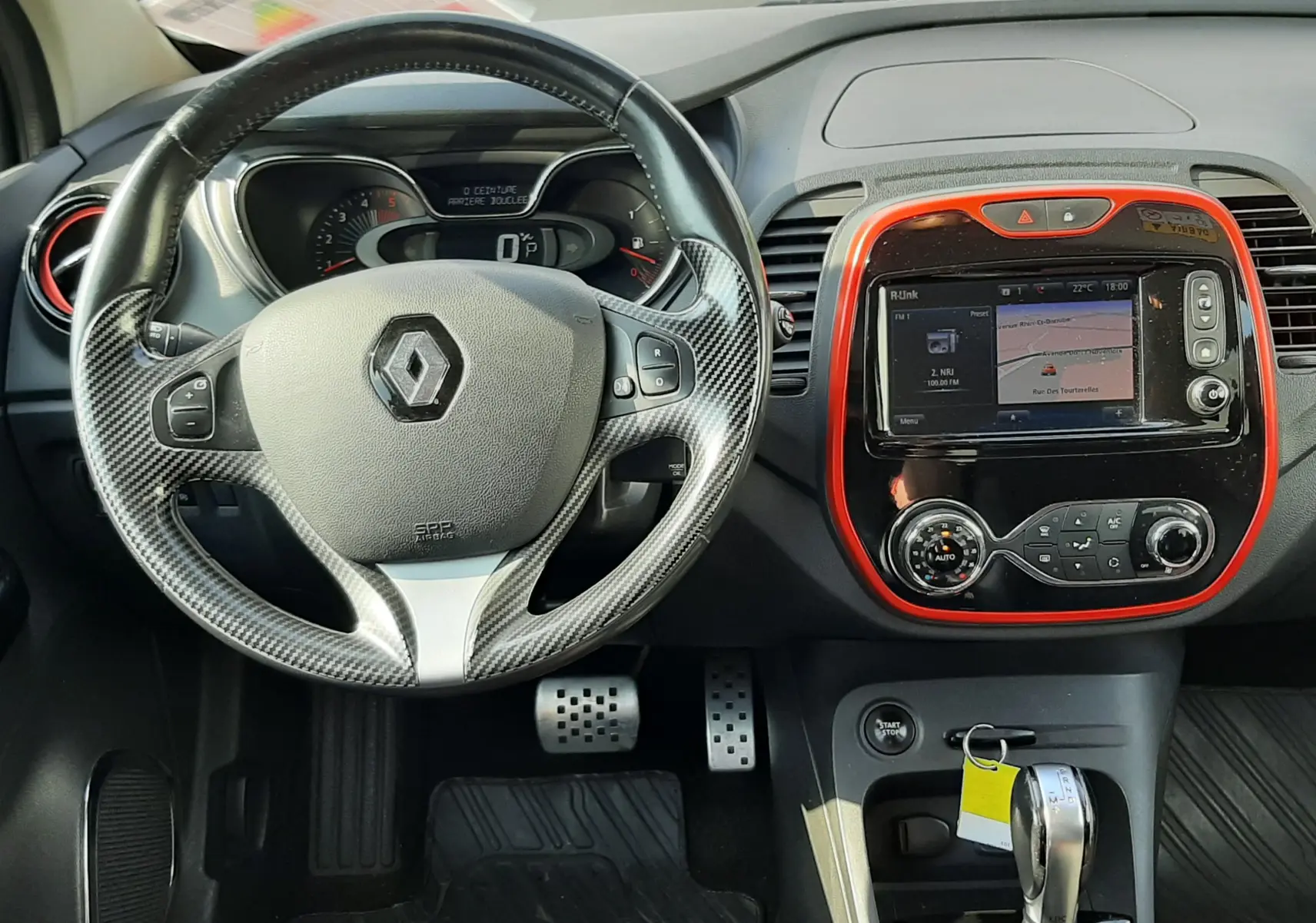Vue intérieure frontale du tableau de bord du Renault Captur gris cassiopée, volant cuir noir, écran tactile avec cadre orange.