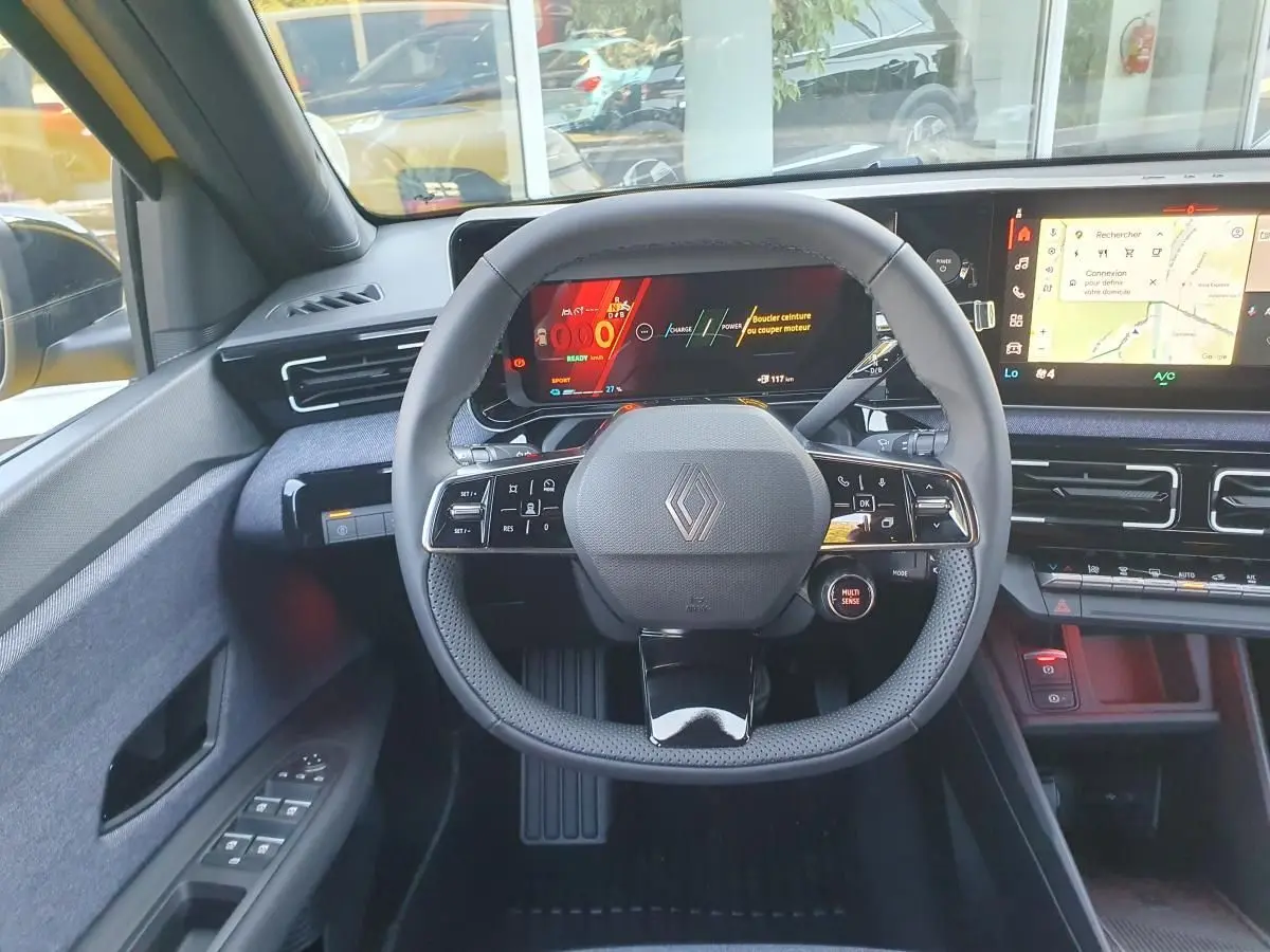 Vue intérieure centrée sur le volant noir de la Renault R5 E-TECH jaune, avec tableau de bord digital et écran tactile.