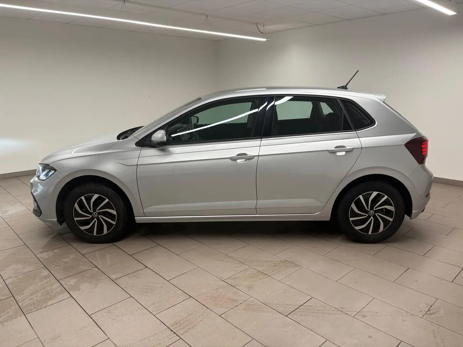 Profil droit d'une Volkswagen Polo 2024 en peinture métallisée Reflet d'argent, avec jantes au design moderne et feux arrière allumés.