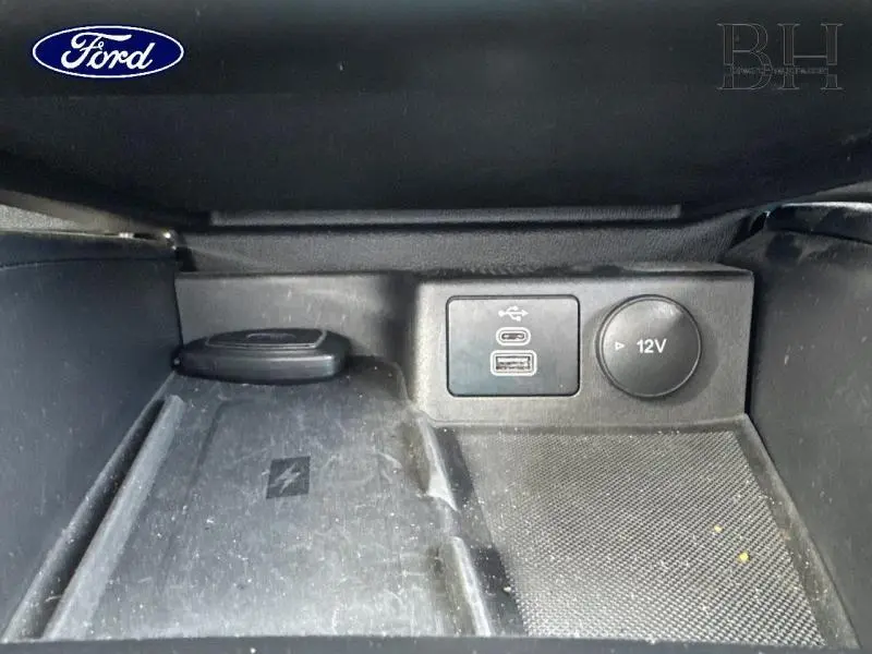 Gros plan sur la console centrale du Ford Focus SW 2023, montrant prises USB et prise 12V dans un intérieur noir.
