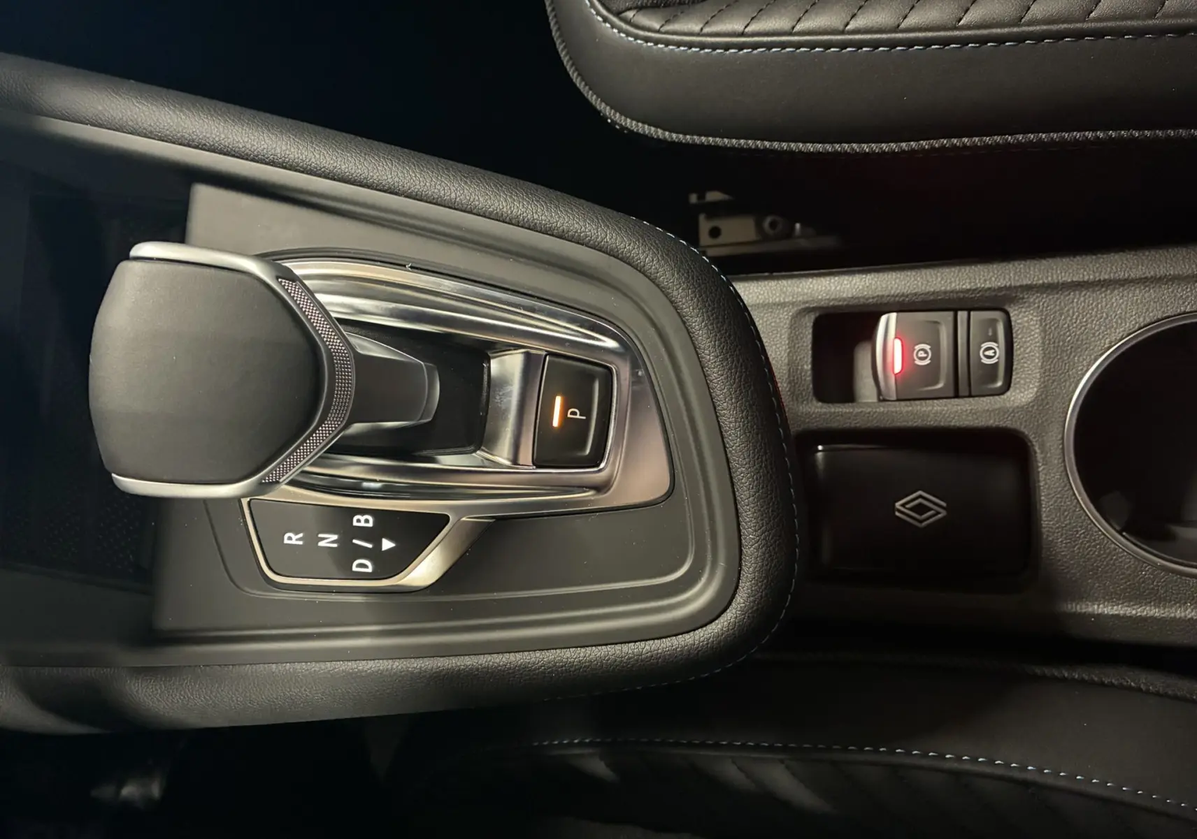 Vue rapprochée de la console centrale du Renault Captur E-Tech hybride 2025, avec levier de vitesse automatique et bouton de frein à main électronique.