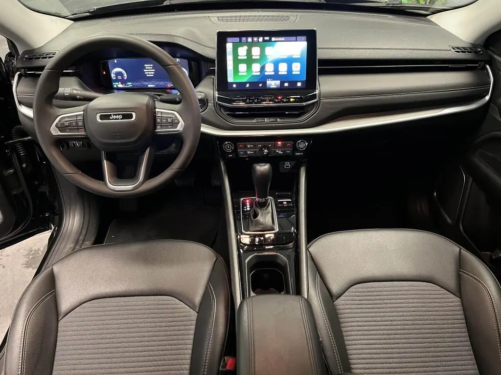 Vue intérieure frontale du Jeep Compass 2024 noir, avec tableau de bord numérique et écran tactile central lumineux.