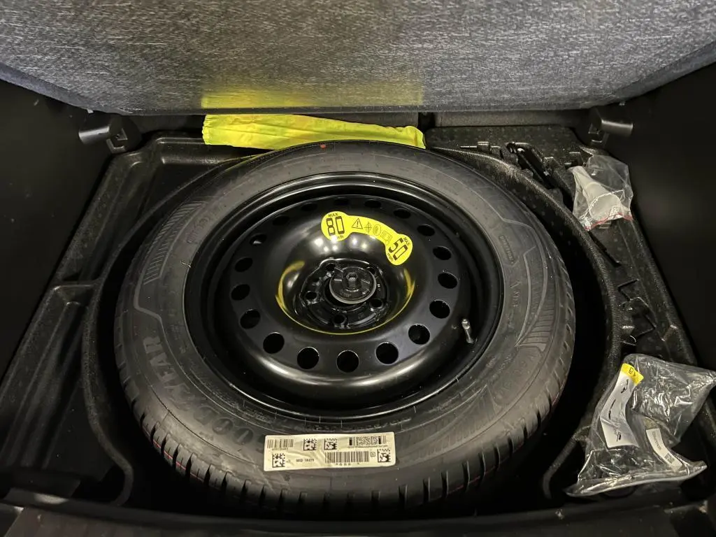 Gros plan sur la roue de secours noire dans le coffre du Jeep Compass 2024, entourée d’accessoires de bord.