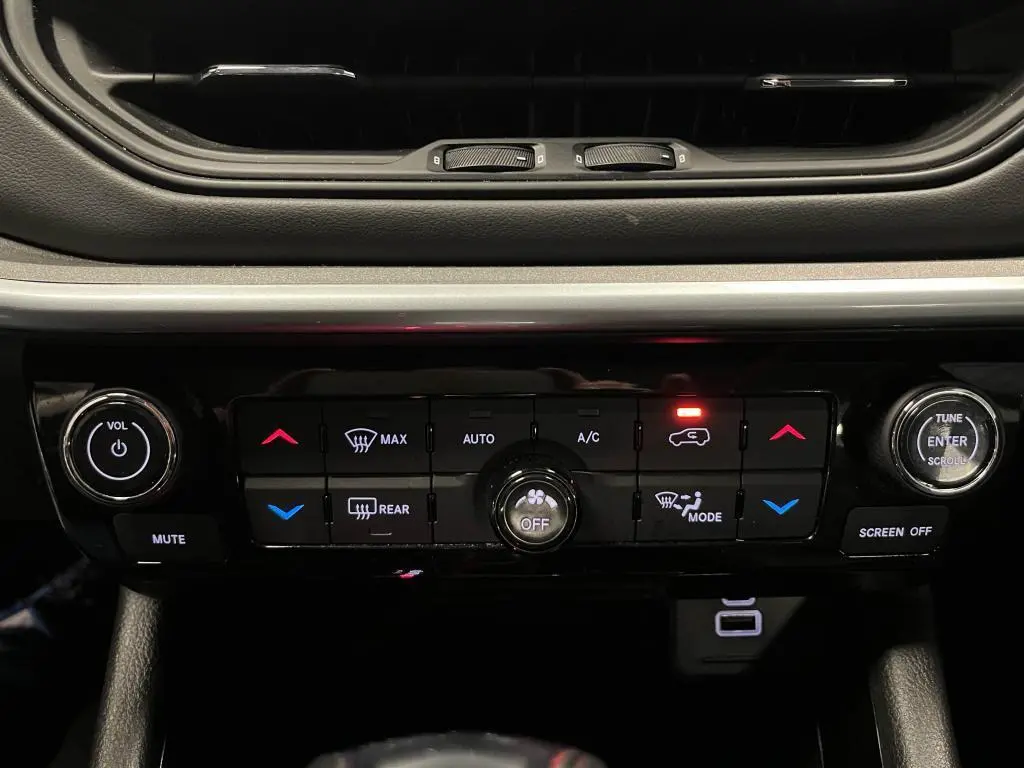 Gros plan sur la console centrale noire du Jeep Compass 2024, avec commandes climatisation et audio éclairées.