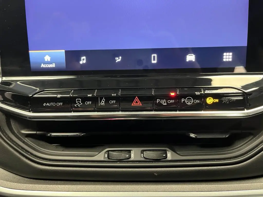 Tableau de bord du Jeep Compass 2024 avec commandes de sécurité et assistance, boutons noirs et écran tactile partiel.