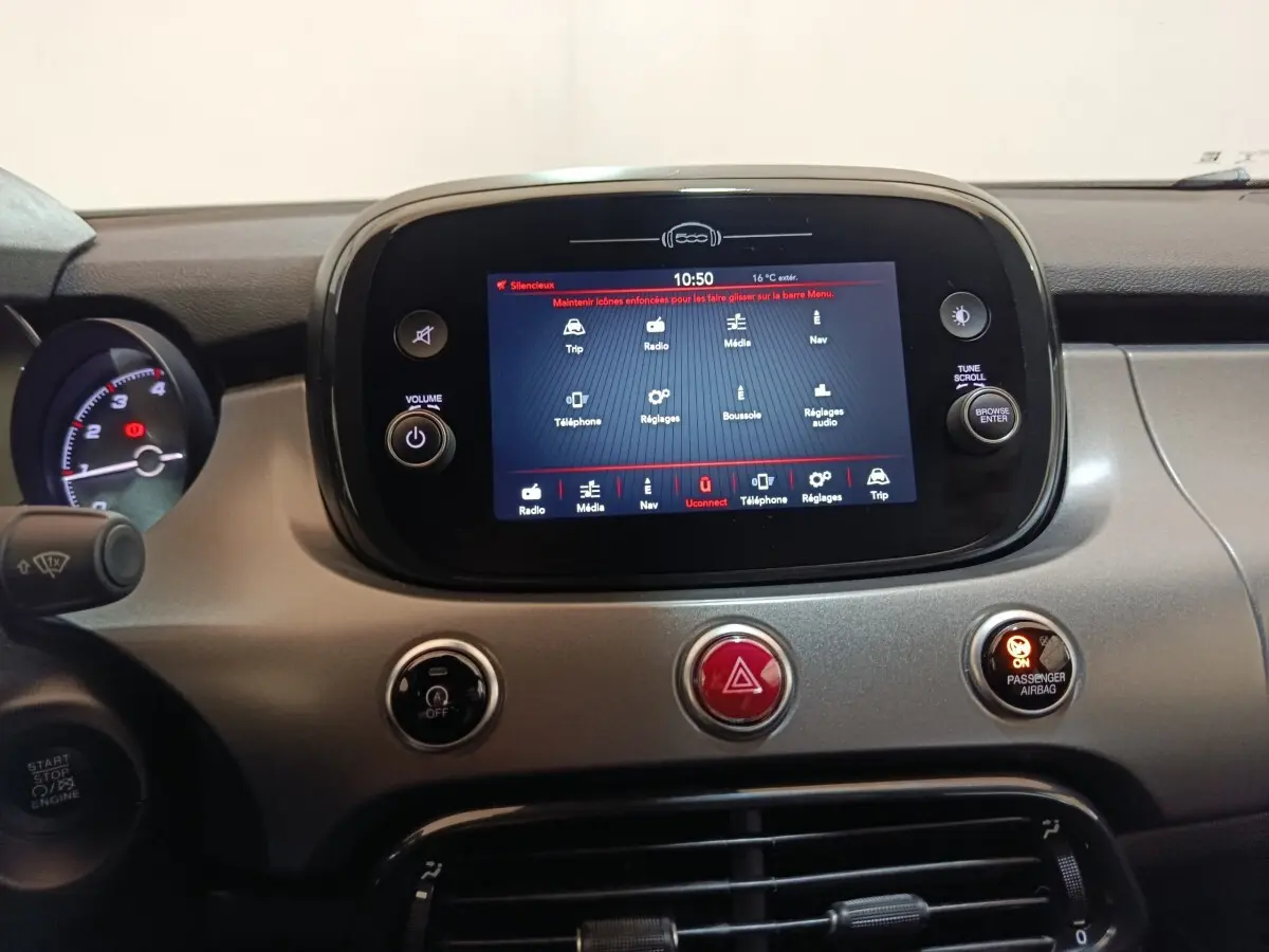 Vue rapprochée du tableau de bord de la Fiat 500X 2021, écran tactile central allumé avec commandes autour.