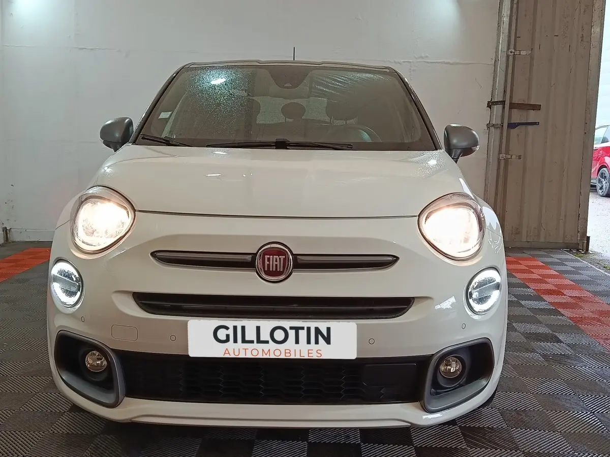 Vue avant d'une FIAT 500X blanche avec phares allumés et feux diurnes LED en intérieur.