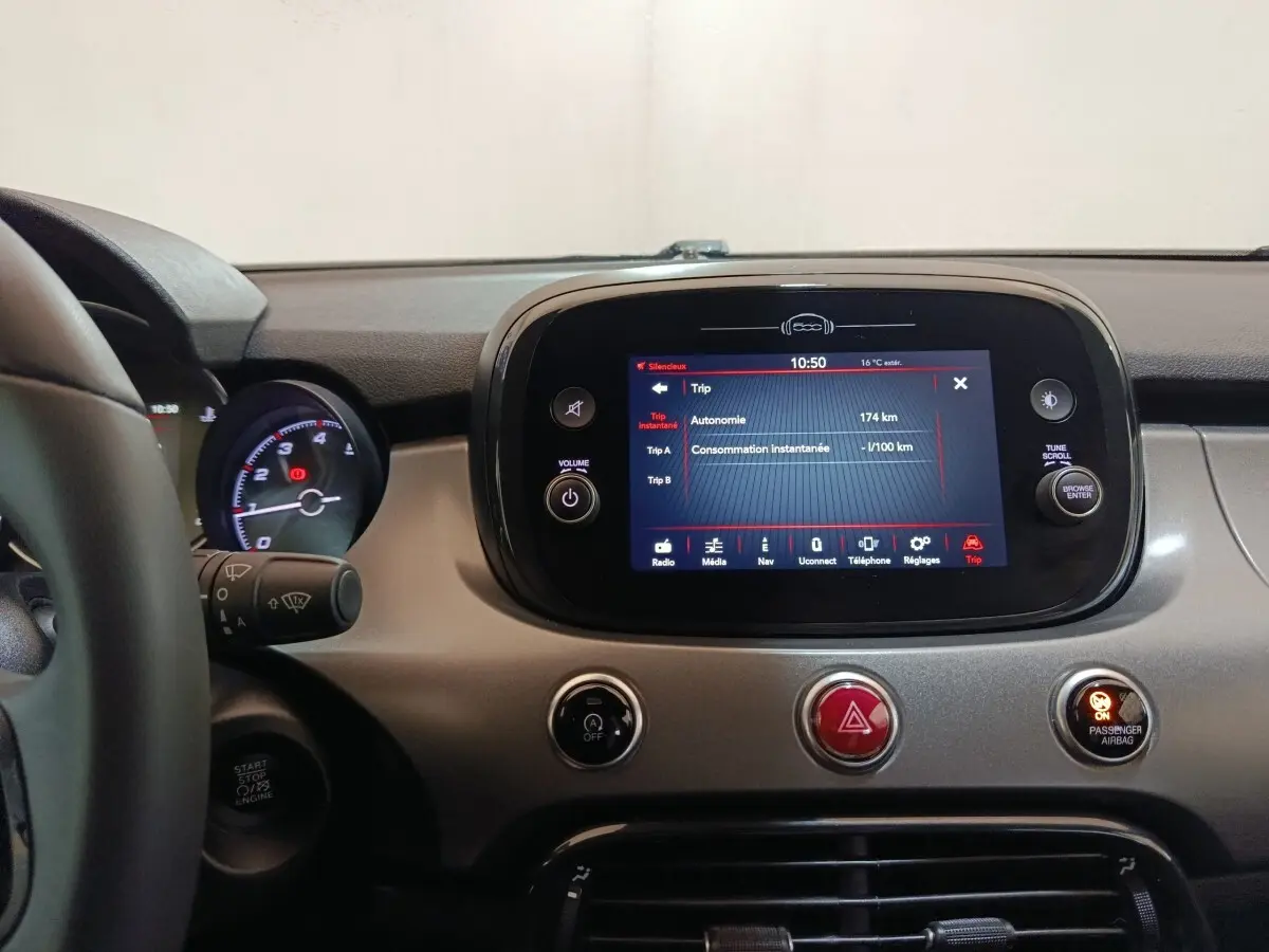 Vue intérieure centrée sur l’écran tactile du tableau de bord gris d’une Fiat 500X noire, avec commandes et volant partiel visible.