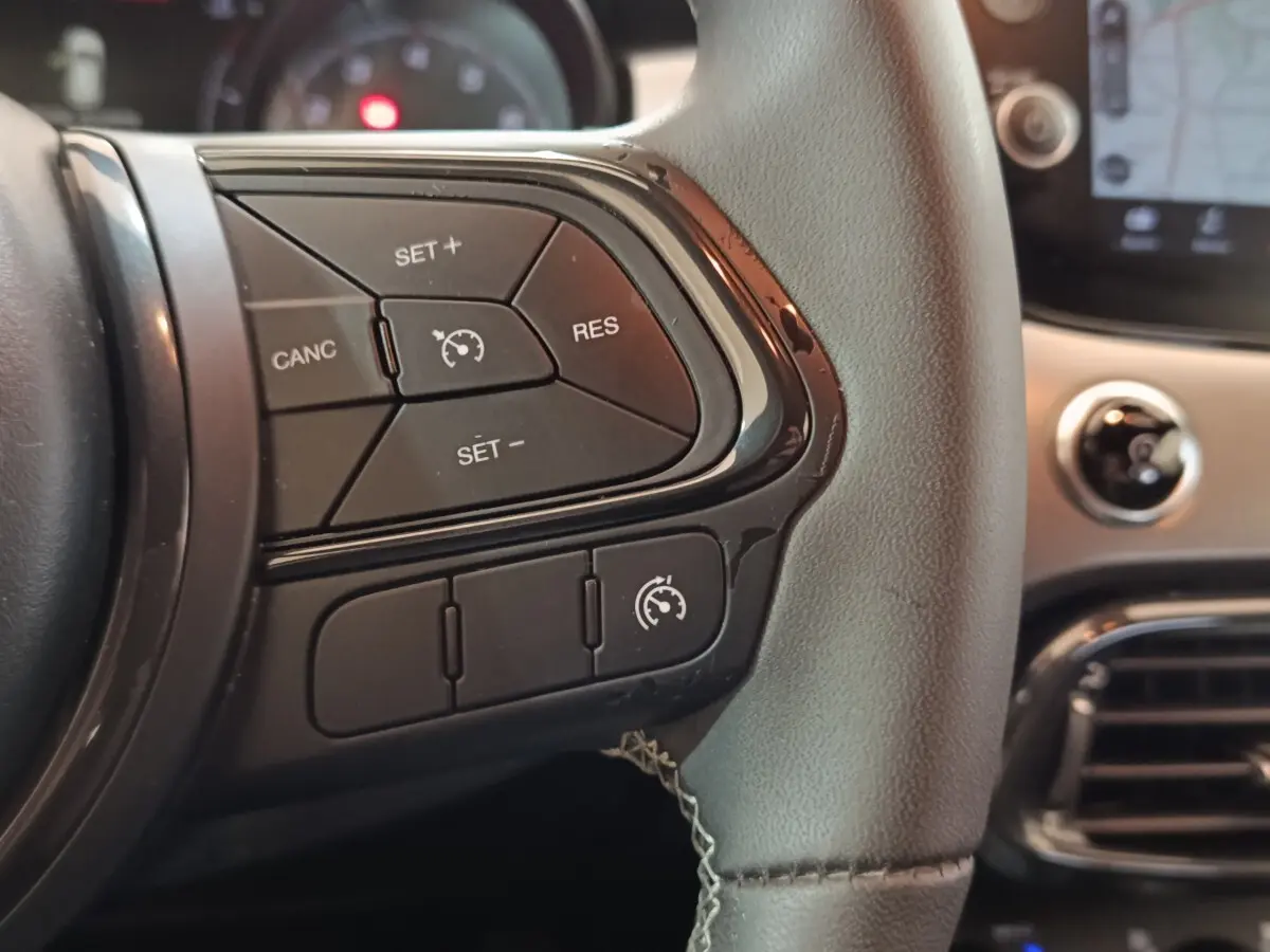 Gros plan sur les commandes de régulateur de vitesse à gauche du volant d’un Fiat 500X noir, intérieur moderne.