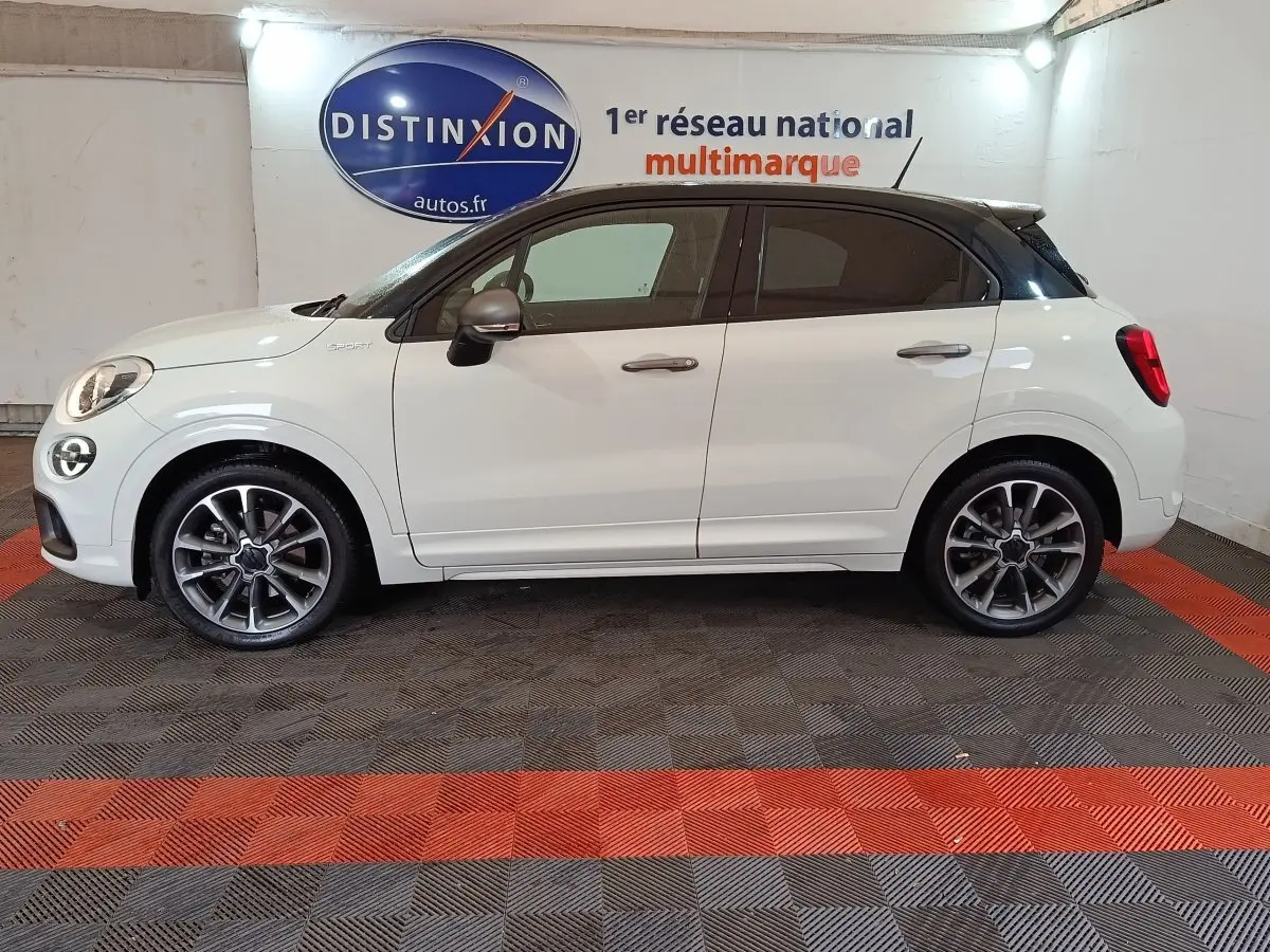 Profil droit d'une FIAT 500X blanche avec toit noir, jantes alliage et logo Sport sur l'aile avant.