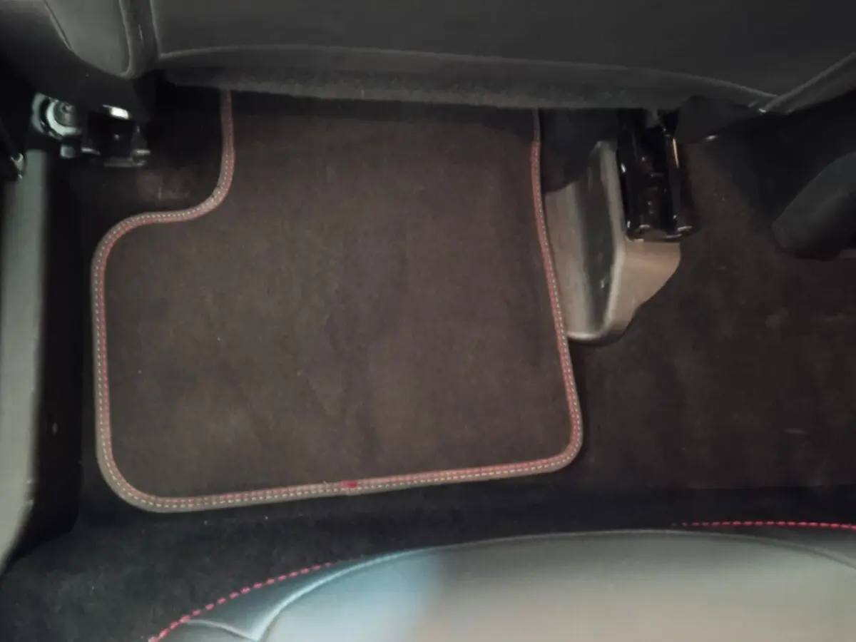 Vue intérieure du plancher côté passager avant de la FIAT 500X noire avec tapis de sol noir et surpiqûres rouges.