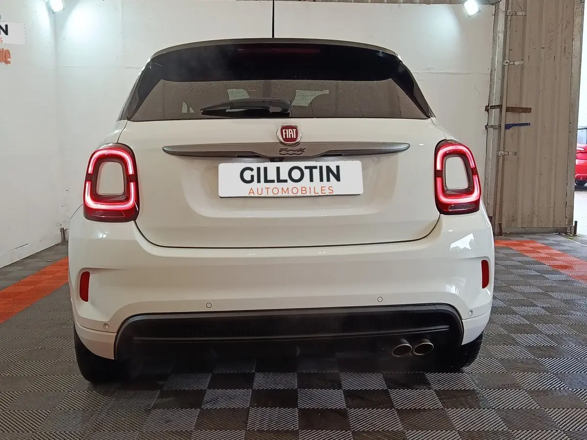 Vue arrière d'une FIAT 500X blanche avec feux arrière LED allumés et double sortie d'échappement à droite.