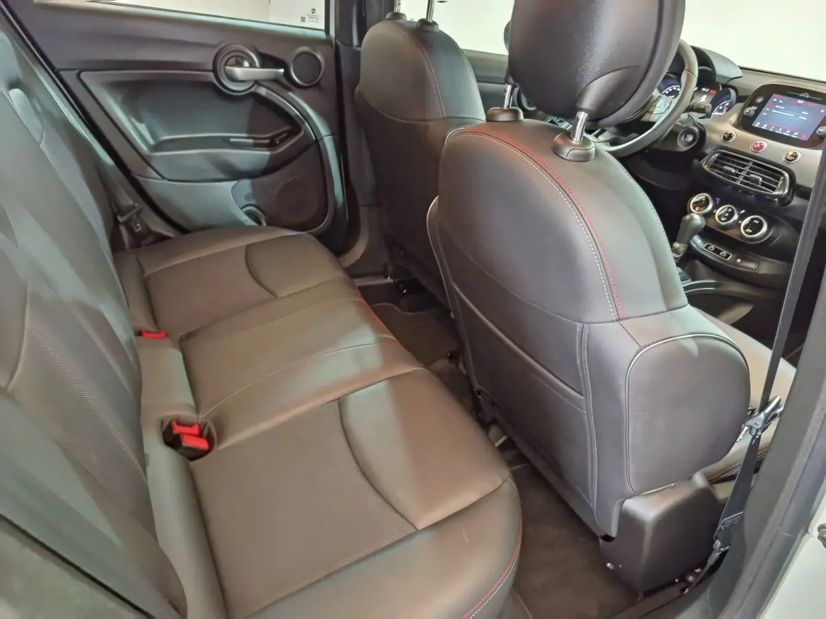 Vue intérieure arrière côté gauche de la Fiat 500X 2021, sièges en cuir noir avec surpiqûres rouges et tableau de bord visible.