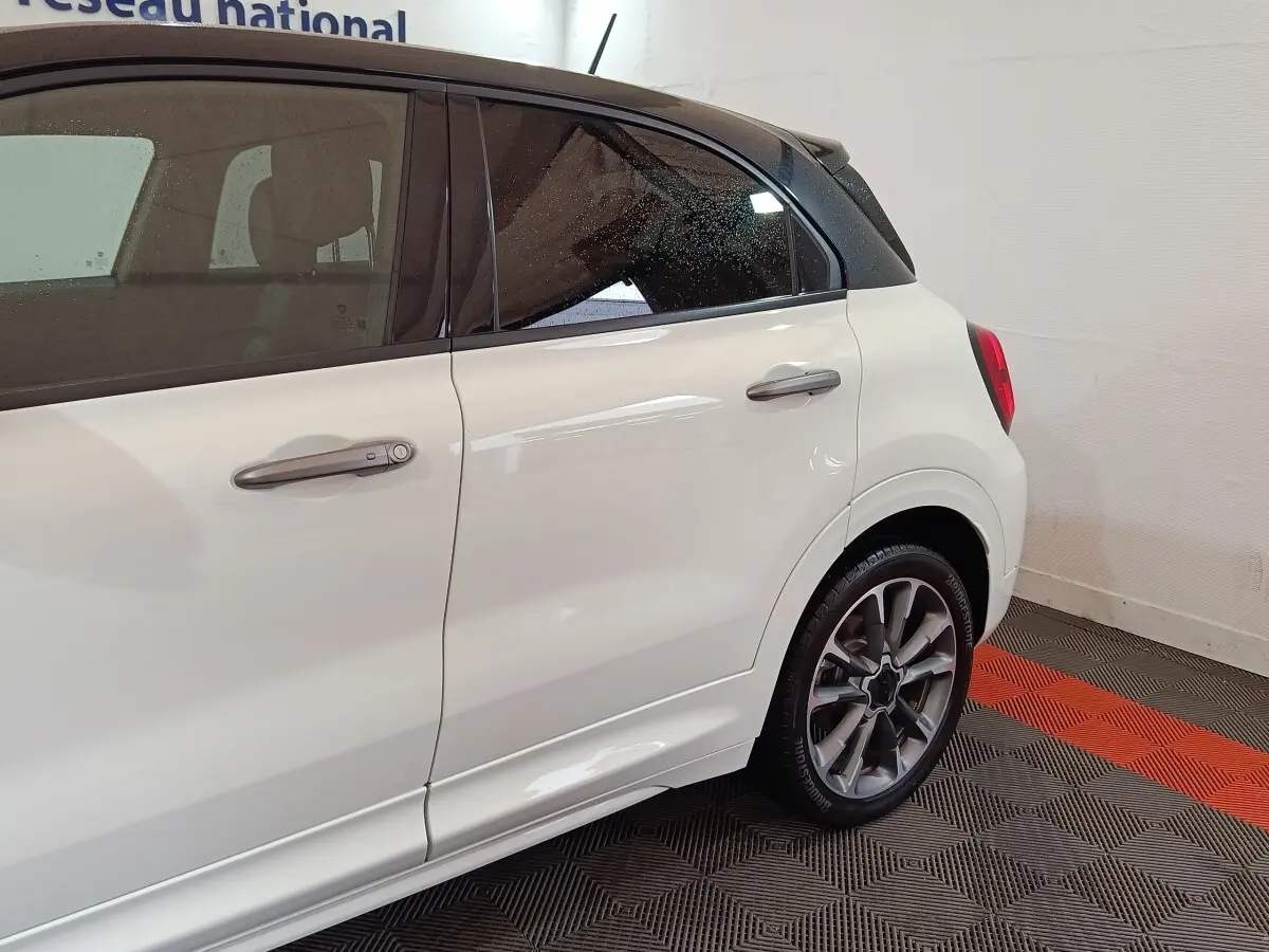 Vue latérale droite d'une FIAT 500X blanche avec toit noir, mettant en valeur les jantes alliage et les poignées de porte chromées.
