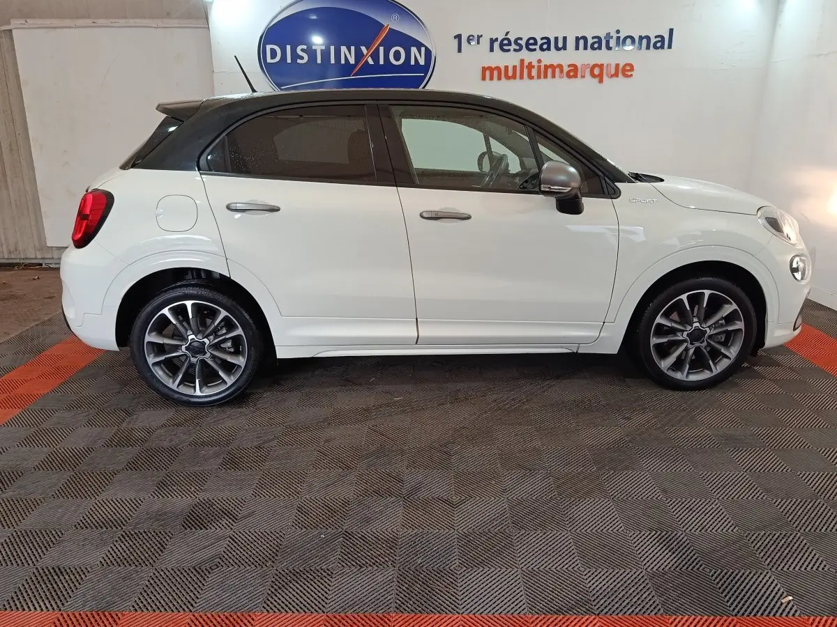 Vue de profil côté gauche d'une FIAT 500X blanche avec toit noir et jantes alliage sport dans un showroom.