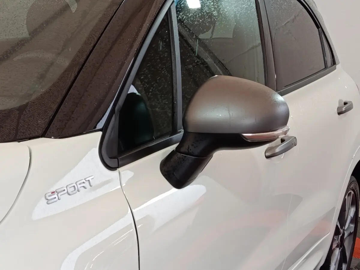 Gros plan sur le rétroviseur côté gauche et l’inscription Sport d’une FIAT 500X blanche avec toit noir.