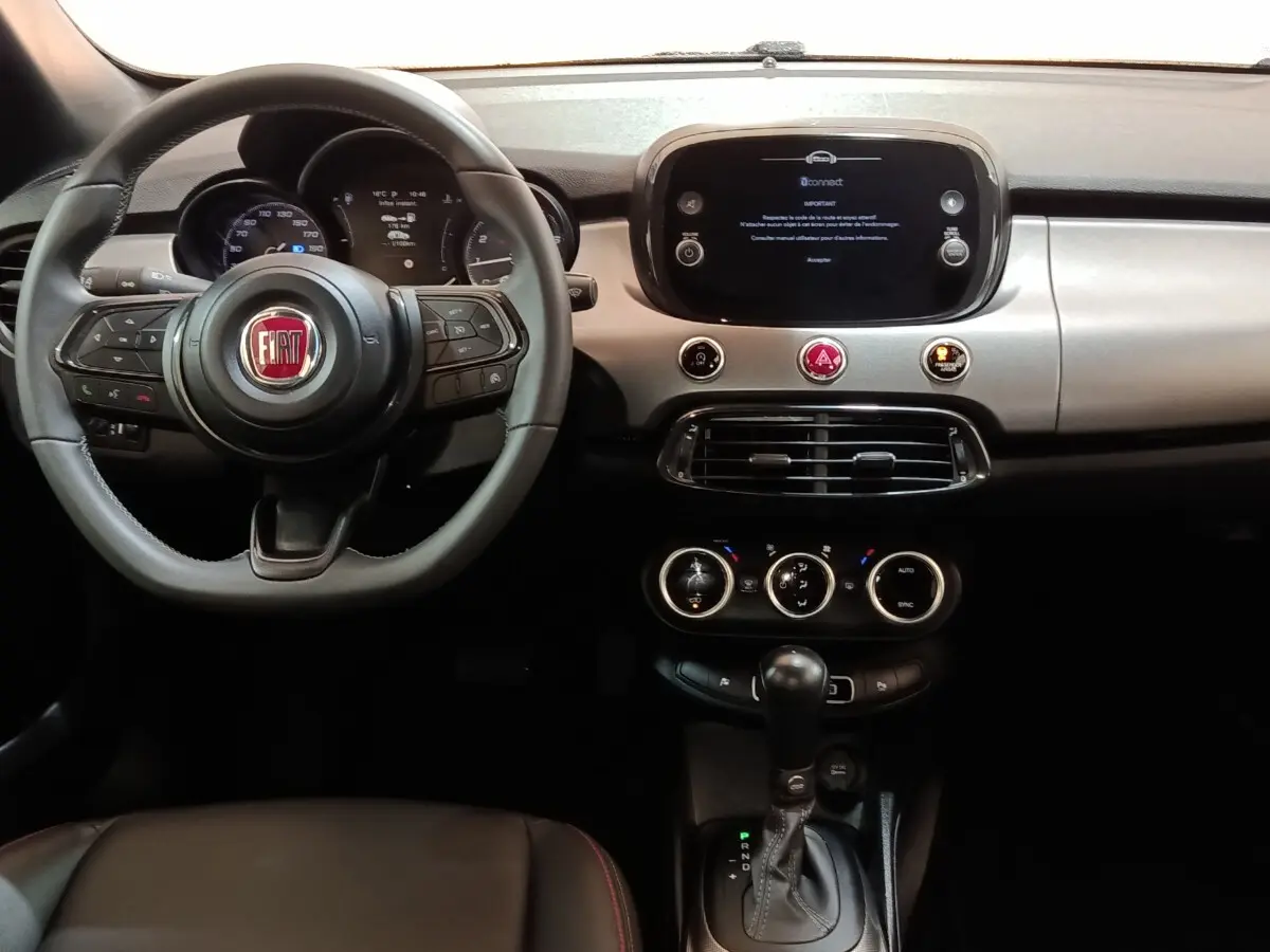 Vue intérieure frontale du tableau de bord noir et volant Fiat 500X avec écran tactile central et commandes intégrées.