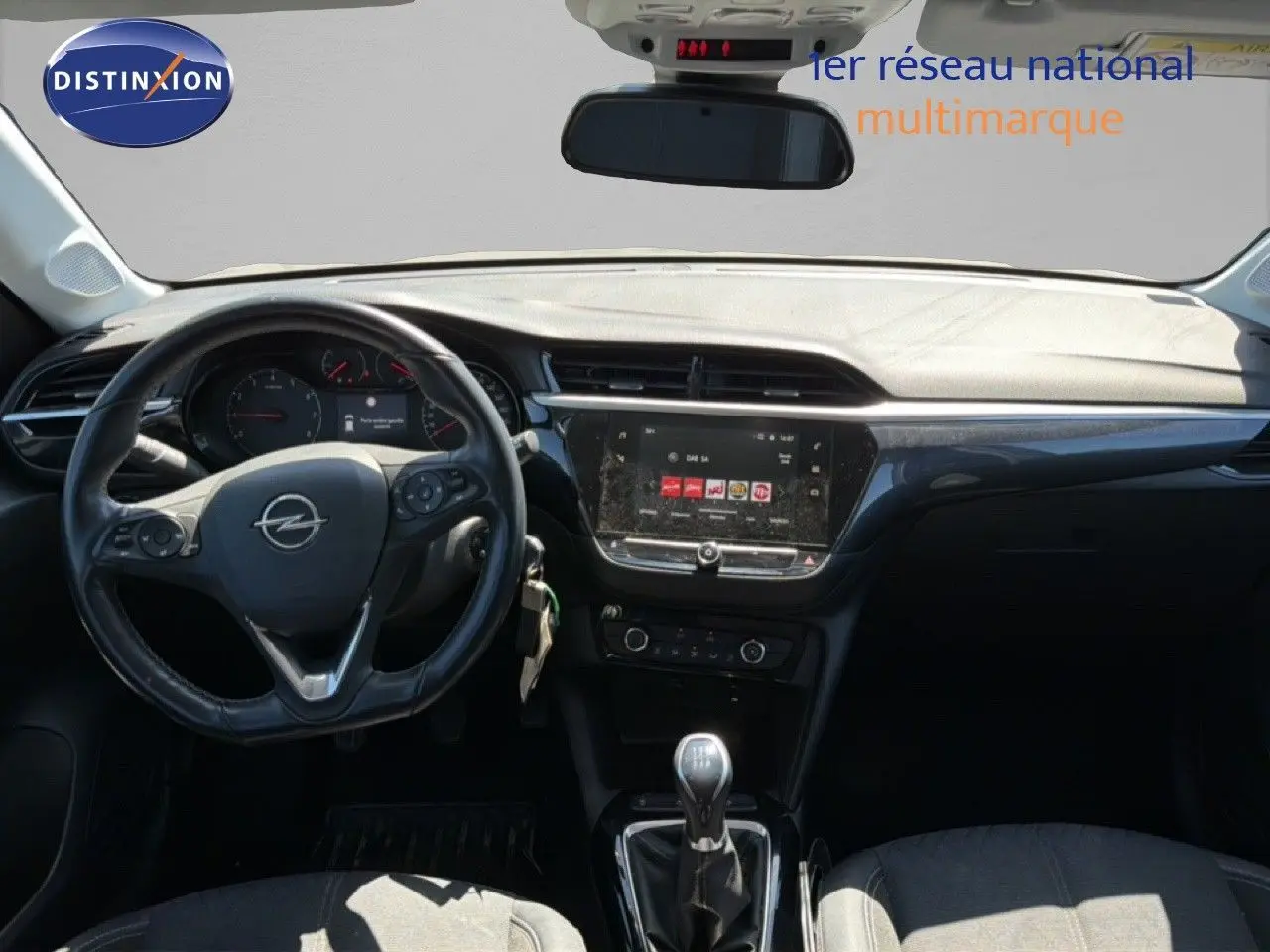 Vue intérieure frontale de l’Opel Corsa gris quartz, montrant le volant, tableau de bord et levier de vitesses manuel.