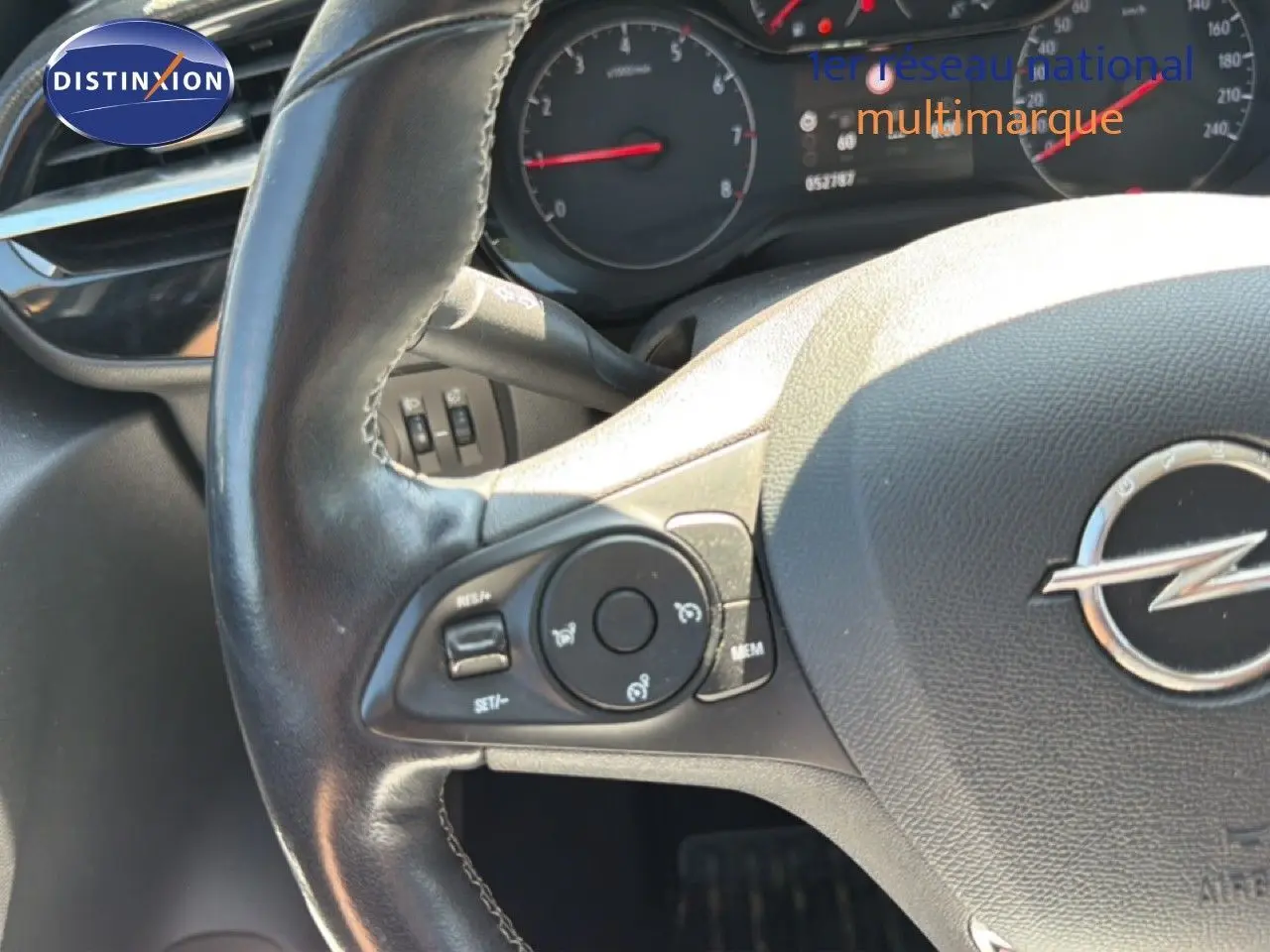 Gros plan sur le volant en cuir noir avec commandes intégrées et logo Opel, tableau de bord partiellement visible.