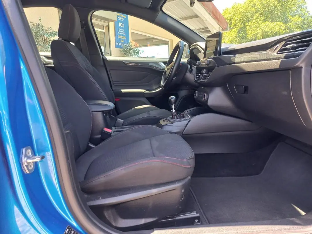 Vue intérieure côté conducteur de la Ford Focus bleu 2019, avec sièges noirs et levier de vitesse manuel visible.