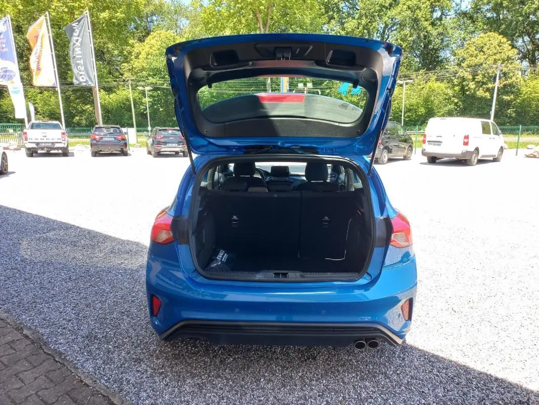 Vue arrière d'une Ford Focus bleue 2019 avec le coffre ouvert, montrant l'espace de chargement et les feux arrière.