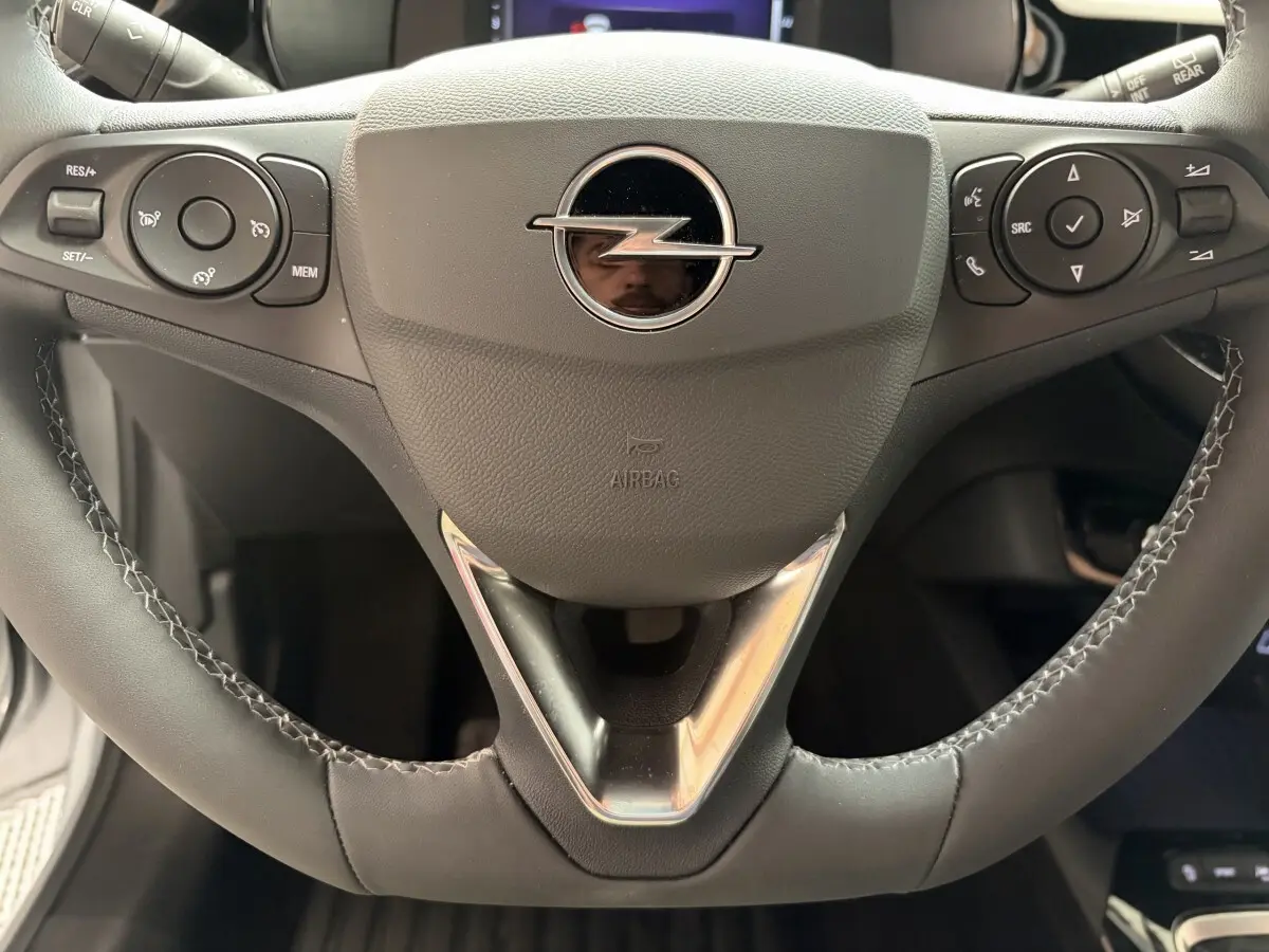 Gros plan sur le volant cuir synthétique noir de l'Opel Corsa 2025 avec commandes multifonctions et logo central chromé.