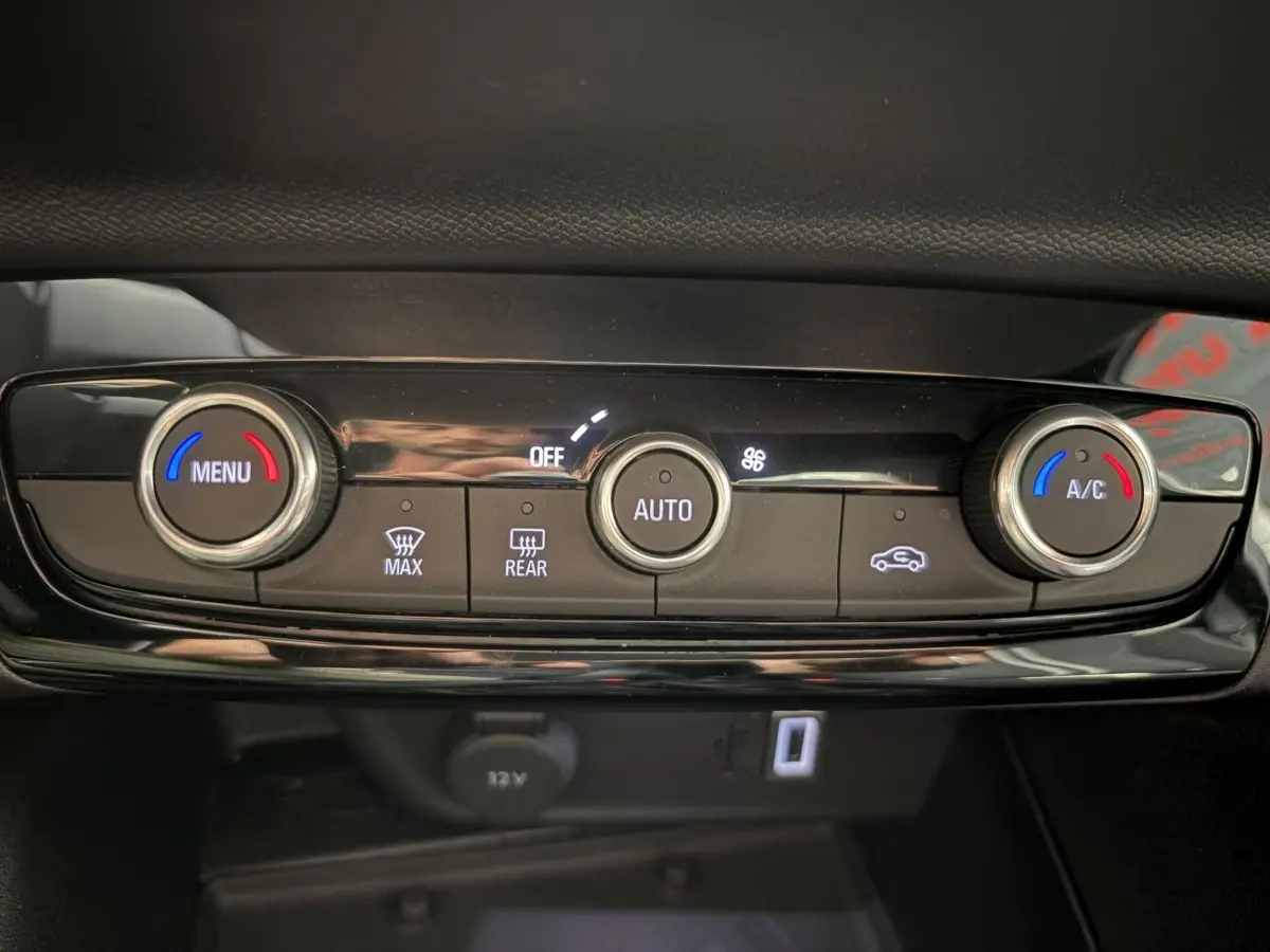 Gros plan sur la console centrale noire de l’Opel Corsa 2025, montrant les commandes de climatisation et prise 12V.