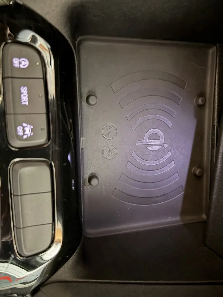 Gros plan sur la zone de recharge sans fil et les boutons de commande noirs brillants dans une Opel Corsa gris clair.
