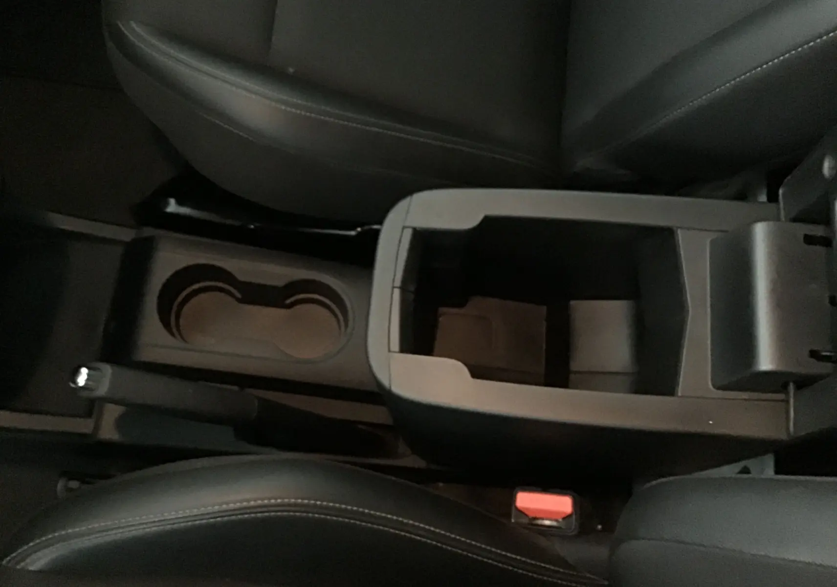 Vue plongeante sur la console centrale noire du Renault Kangoo blanc 2022, avec porte-gobelets et accoudoir ouvert.