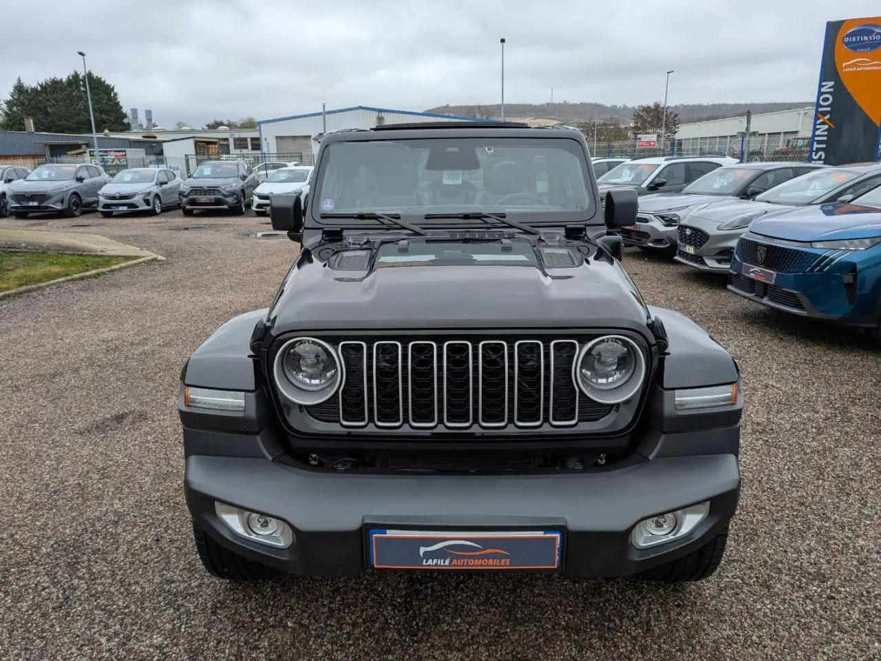 Vue de face du Jeep Wrangler noir avec calandre à sept fentes et phares ronds LED, sur parking extérieur.