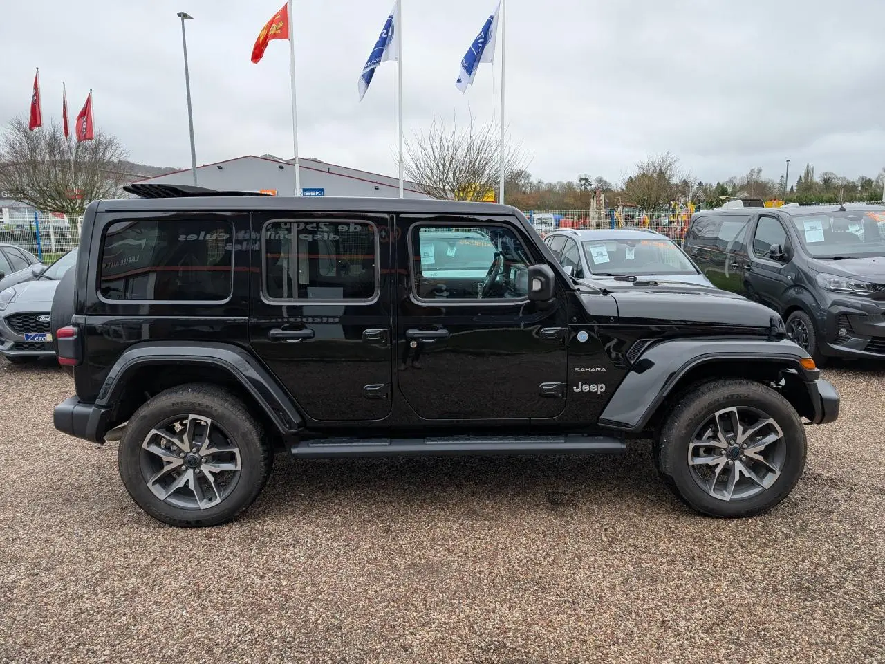 Vue de profil côté gauche d'un Jeep Wrangler Unlimited Sahara noir avec jantes alliage 20 pouces et marchepieds.